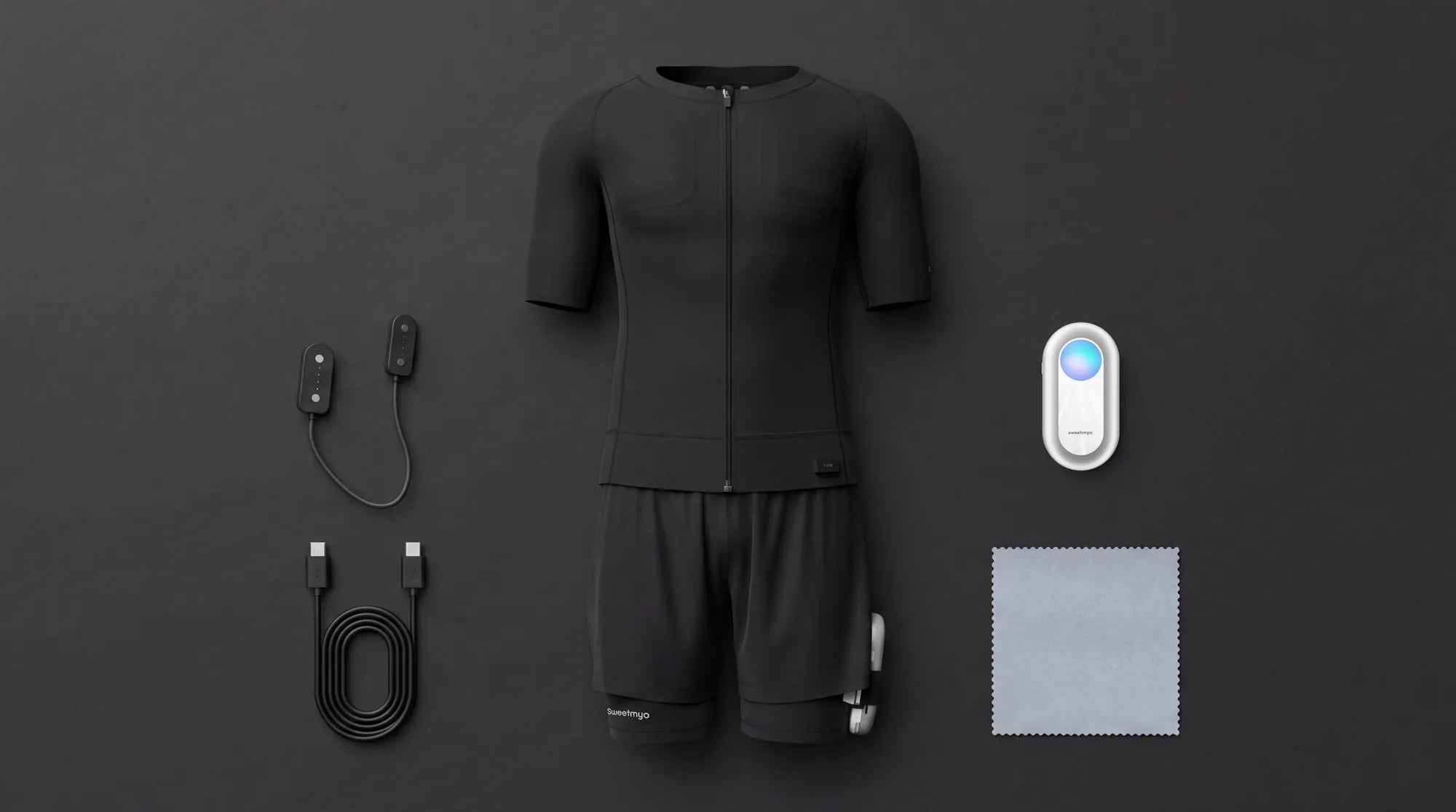 Black Sweetmyo EMS suit top and shorts with controller, charging cables, and cleaning cloth arranged on a dark surface