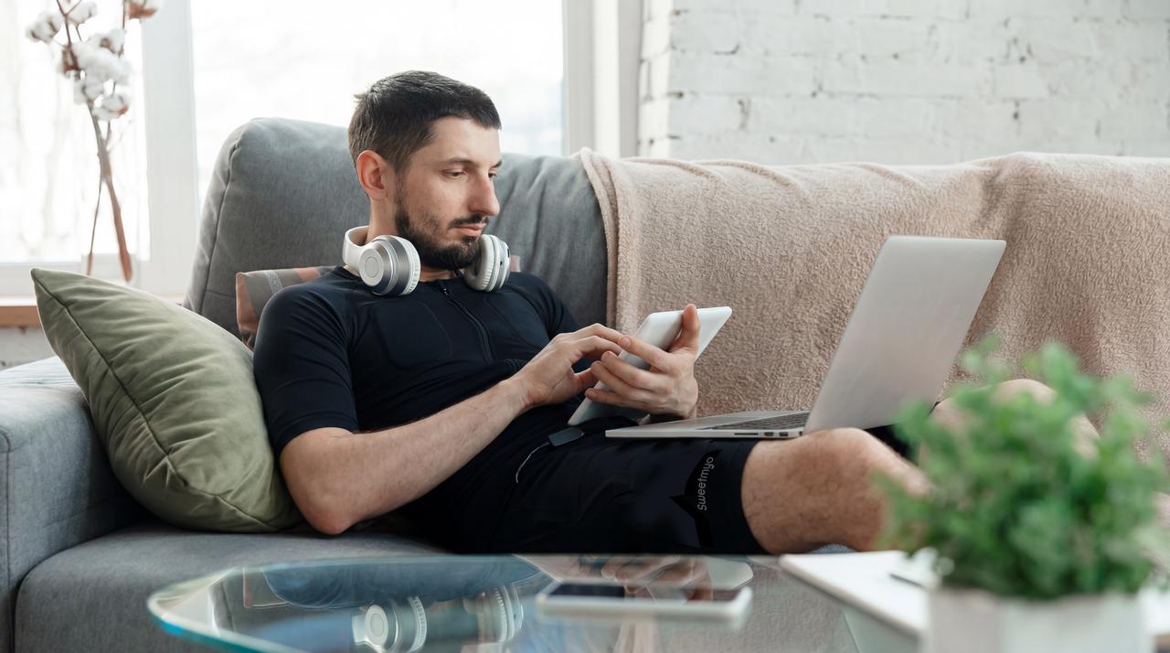 Man wearing a Full-Body EMS Suit relaxing on a sofa with headphones